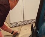 Using homemade vacuum attachment to clean under a refrigerator.