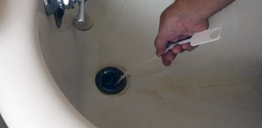 Using a drain stick to clean a bathtub drain.