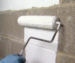 Rolling masonry waterproofer on concrete block basement wall.