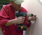 Using a cordless drill to attach drywall screws to drywall wall.