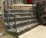 Curved brick porch steps with wrought iron railing on front of house.