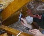 Man with smartphone tracking down roof leak in attic.