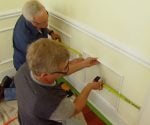 Installing white faux wainscoting on yellow walls in living room.