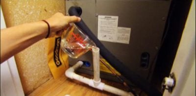 Pouring a cup of bleach in an air conditioner drain line to kill algae and prevent clogs.