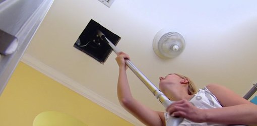 Using a vacuum cleaner crevice attachment to clean a bathroom vent fan.