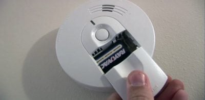 Opening the cover on a smoke alarm to change the battery.
