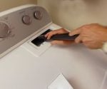 Using a vacuum cleaner crevice tool to remove lint inside a dryer.