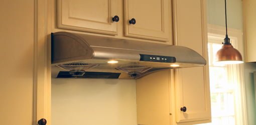 Stainless steel range hood over stove with painted cabinets.